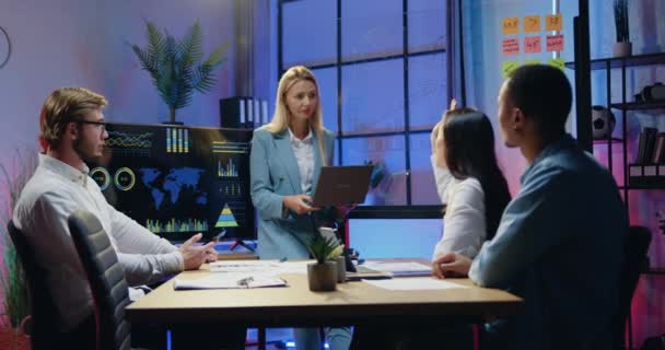 Krásná sebevědomá profesionální blondýnka vedoucí týmu vysvětlující prezentaci na digitálním displeji pro pozorné motivované různé podřízené během setkání ve večerní kanceláři — Stock video