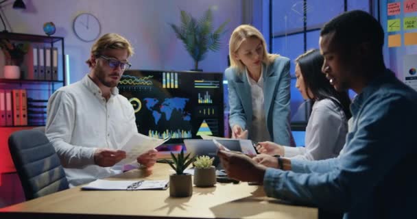 Office work concept where attractive confident smart motivated multicultural workmates browsing paper reports with charts during joint meeting in workroom in the evening — Stock Video