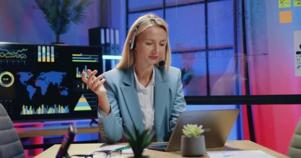 Distant office work where attractive positive confident high-qualified female manager in headset holding online meeting with fellow and explain details of joint work in the evening — Stock video