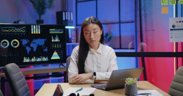 Attraktiv positiv säker lugn skicklig asiatisk kvinna sitter framför kameran i modern kväll arbetsrum och tittar med uppriktigt leende, närbild porträtt — Stockvideo