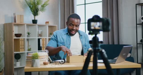 Guapo sonriente feliz joven barbudo afroamericano blogger grabación proceso de desembalaje en la cámara para audinece Internet y mostrando nuevo teléfono inteligente de la caja — Vídeos de Stock