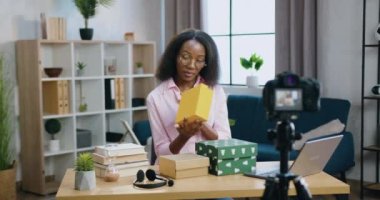 İnternet kanalı için video kaydında hediye kutuları gösteren sevimli gülümseyen mutlu Afro-Amerikan kadının blog konsepti