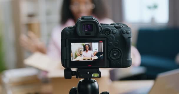 Se concentrant sur la caméra où belle sourire jeune femme afro-américaine heureuse dans des lunettes enregistrement vidéo pendant le processus de déballage pour le public Internet — Video