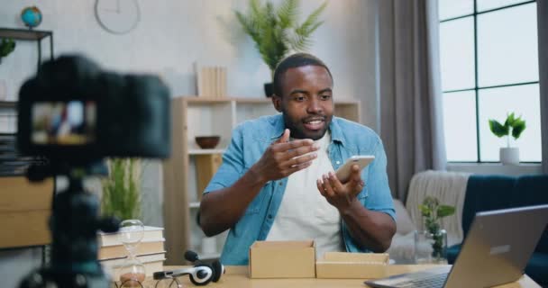 Ймовірно позитивний щасливий відомий бородатий афроамериканський блогер розповідає про нові можливості смартфона на камеру для інтернет глядачів на домашньому тлі інтер'єру — стокове відео