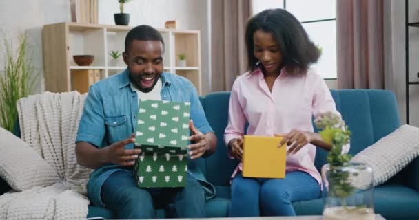 令人惊讶的家庭，在那里迷人而兴奋的笑着的年轻非洲裔美国夫妇打开礼品盒，看到礼品盒时大开眼界，眼前的景象 — 图库视频影像