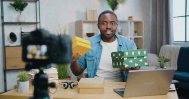 İyi görünümlü, gülümseyen, sakallı, genç, Afro-Amerikalı adamın ön görüntüsü. İnternet kanalı için video bloğu kaydederken elinde hediye kutuları tutan adam.