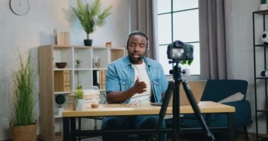 Çekici özgüvenli sakallı Afrikalı Amerikalı blogcu, modern apartmandan izleyiciler için kulaklık takıyor.