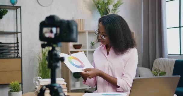 Красива впевнена позитивна молода афроамериканська жінка-тренер в окулярах пояснює схему під час онлайн-потоку на камеру з домашньої студії, вид спереду — стокове відео
