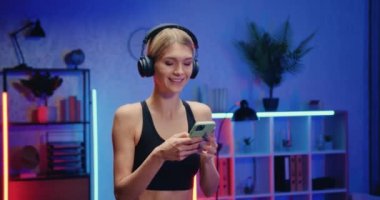 İyi görünümlü, fit, kulaklıklı genç bir sarışın koşu pistine çıkıyor ve telefon listesinden müzik seçiyor.