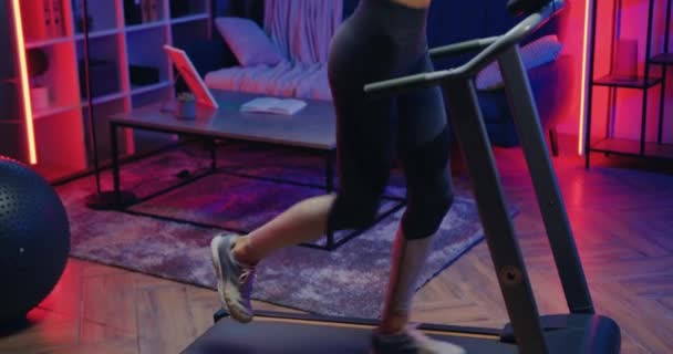 Schöne sportlich schlanke junge Läuferin in Sportbekleidung joggt abends beim Training zu Hause auf dem Laufband, Zeitlupe — Stockvideo