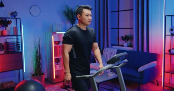 Handsome confident sportive asian guy in training clothes walking on running track during evening home workout,healthy lifestyle concept — Stock Video