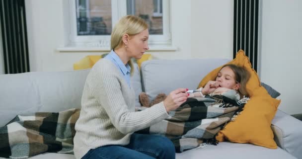 Aantrekkelijke opgewonden liefdevolle moeder verzorgen van haar zieke overstuur tienerdochter die liggend op comfortabele bank en hoesten, griep of angina pectoris concept — Stockvideo