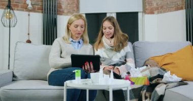 Hoş gülümseyen genç kız portresi. Öksürük ve oturma odasındaki rahat kanepede oturup ilginç uygulamaları izlemek için tablet bilgisayar kullanan pozitif ve sevgi dolu annesi.