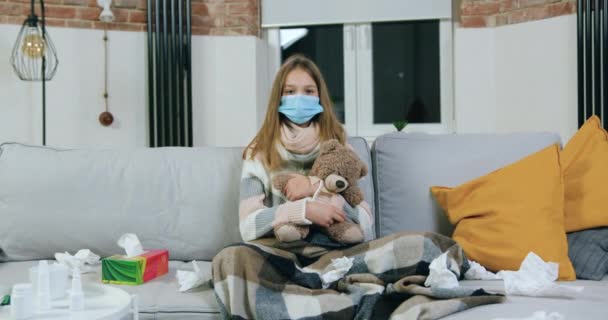 Досить нещасна хвора дівчина-підліток у медичній масці, сидячи на м'якому дивані у вітальні на домашній самоізоляції під час хвороб, хвороб та концепції охорони здоров'я, концепція коронавірусу — стокове відео