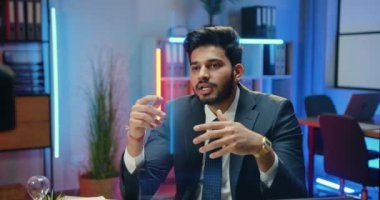 Çekici, kendine güvenen, takım elbiseli, profesyonel ofis koçu. Gece aydınlatmalı ofis odasından online izleyiciler için iş eğitimi alıyor.