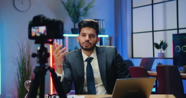 Ελκυστική αυτοπεποίθηση σκόπιμη γενειοφόρος επιχειρηματίας με κοστούμι κάθεται μπροστά από την κάμερα στο γραφείο το βράδυ κατά τη διάρκεια της εγγραφής βίντεο για το επιχειρηματικό κανάλι — Αρχείο Βίντεο