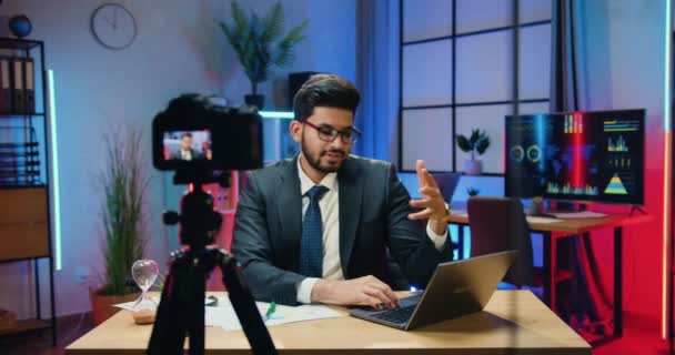 Webinaire en ligne concept où beau homme d'affaires barbu expérimenté en lunettes porte costume élégant assis devant la caméra dans le bureau du soir et parler avec le public — Video