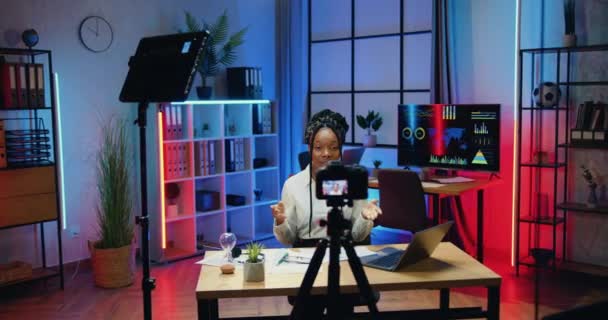 Kamera fotografering på vackra framgångsrika smarta professionella afrikanska affärskvinna i elegant slitage som spelar in video för hennes internet kanal på videokamera på kvällen kontor bakgrund — Stockvideo