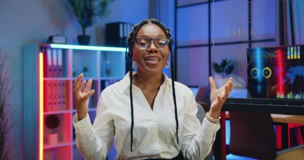 Gyönyörű mosolygós elégedett képzett sikeres afro-amerikai üzletasszony szemüvegben beszél a kamerába az esti irodában, és tapsoló kezét a beszélgetés befejezése után — Stock videók