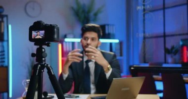 İyi görünümlü, profesyonel, yetenekli, sakallı iş adamı. Takım elbiseli, akşam çalışma odasında iş kanalı için kameraya video kaydediyor.