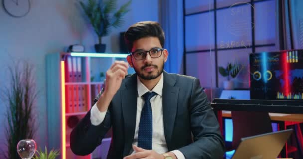 Portret van sympathieke zelfverzekerde positieve ervaren bebaarde zakenman in formele slijtage in bril die poseren op camera op nacht verlichte werkkamer achtergrond — Stockvideo