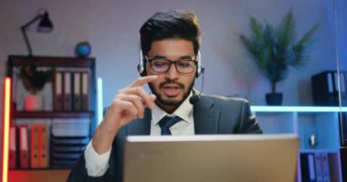 Ofisteki iş arkadaşlarıyla video görüşmesinde dosya ile birlikte gösteren kulaklıklı, kendine güveni tam, modern sakallı bir ofis çalışanına bilgisayar üzerinden ateş etmek.