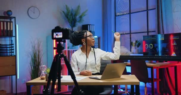 Красивая, уверенная в себе опытная, стильная африканская бизнесвумен проводит онлайн-конференцию с использованием камеры в вечернем офисе и объясняет результаты импорта и экспорта товаров — стоковое видео