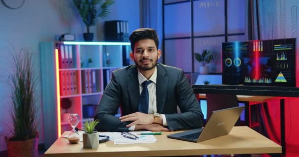 Attrayant positif expérimenté intelligent homme d'affaires barbu élégant posant à la caméra sur son lieu de travail dans le bureau du soir, vue de face, ralenti — Video