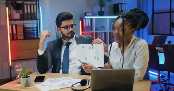 Gut aussehende selbstbewusste Verantwortliche motivierten diverse Geschäftsleute, während eines Videochats mit Partnern im Abendbüro vor laufender Kamera das Diagramm zu erklären. — Stockvideo