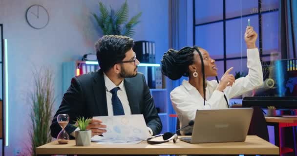 Réussite probable créatif intelligent qualifié multiethnique hommes et femmes collègues d'affaires remue-méninges sur le projet de démarrage conjoint en utilisant des rapports papier et des informations sur ordinateur portable dans le bureau sombre — Video