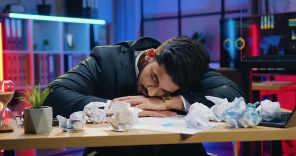 Крупным планом симпатичного утомленного переутомленного бородатого бизнесмена, который спит на столе с компьютером и смятыми бумагами в офисе в последнее время — стоковое видео