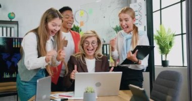 Dizüstü bilgisayara bakıp ofisteki brifing masasında online başarısını kutlayan dört başarılı bayan meslektaşın takımı heyecanlı ve mutlu..