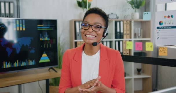 Gioioso elegante operatore femminile di call center in cuffia sta parlando a macchina fotografica online, sorridendo — Video Stock