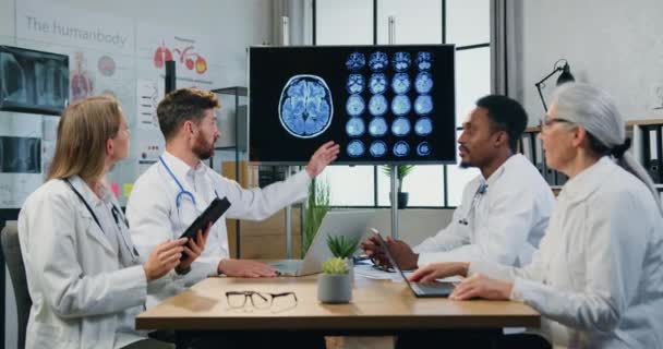 Likable confident purposeful diverse male and female medical team of neurologists holding joint consultation in medical room about patients diagnosis using mri brain — Stock Video