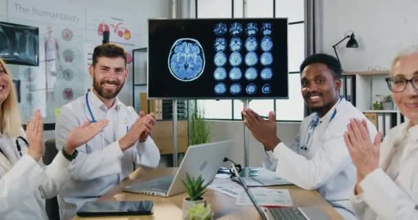 Atractivo sonriente exitoso experimentado multiétnico hombres y mujeres médicos aplaudiendo de la mano en la cámara en la sala de la clínica, concepto de medicina — Vídeo de stock