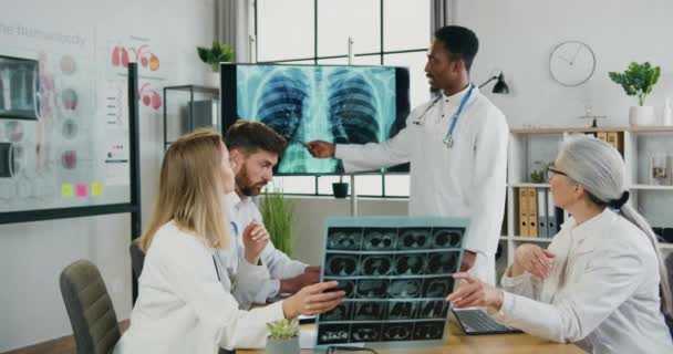 Fluxo de trabalho na clínica, onde atraentes médicos multiétnicos qualificados e confiáveis são aquecidos com a radiografia de tórax e a varredura dos pulmões dos pacientes durante a reunião conjunta — Vídeo de Stock
