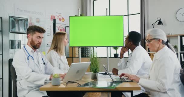 Aanzienlijke verantwoordelijke ervaren slimme multiculturele team van artsen die samenwerken in het medisch kantoor en gebruik maken van digitale display met groene chroma key screen — Stockvideo