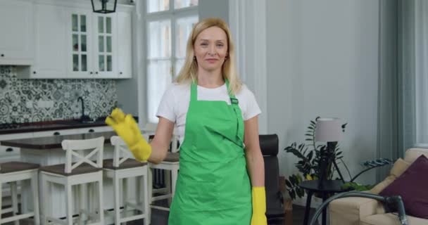 Probable souriant satisfait adulte blond femme-travailleur de l'entreprise de nettoyage montrant dans le geste de la caméra ok après avoir fini nettoyer la maison du client — Video