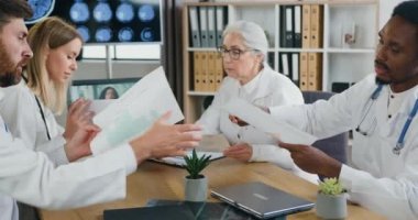 Klinikteki ortak toplantı sırasında farklı tıbbi raporlarla birlikte çalışan çok ırklı, maksatlı, makul yoğunlukta deneyimli doktorlar.