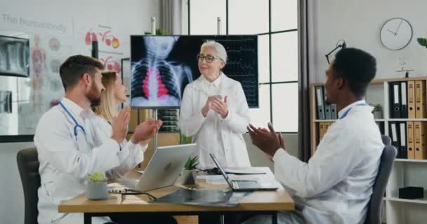 Des médecins multiculturels attrayants et positifs avec une femme médecin-chef applaudissant après la fin d'une réunion efficace dans un cabinet médical moderne — Video