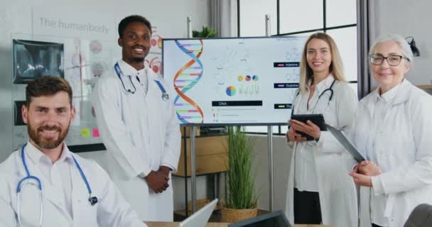 Retrato de boa aparência sorrindo bem sucedido experiente equipe multiétnica de médicos que posando na câmera no escritório de clínica moderna — Vídeo de Stock