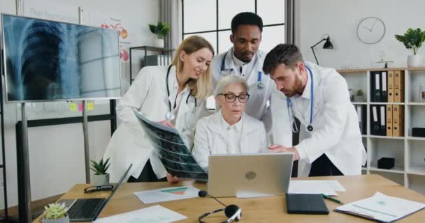 Pewny siebie pozytywny, wysoko wykwalifikowany, zróżnicowany zespół lekarzy pracujących razem podczas spotkania w gabinecie medycznym i czytających wyniki ekspertyz na ekranie komputera — Wideo stockowe
