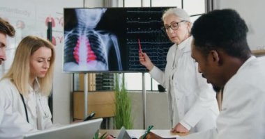İyi görünümlü deneyimli, ilgili, çok ırklı doktorlar modern tıp odasındaki dijital ekranda kalp atışlarının zayıfladığı hastaların sonuçlarını tartışıyorlar.