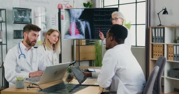 Bela confiante bem sucedida médica madura explicando radiografia de tórax, varredura de pulmões e batimentos cardíacos na tela digital para estagiários masculinos e femininos multiétnicos motivados — Vídeo de Stock