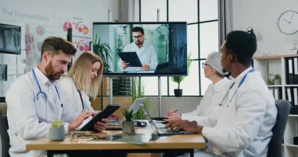 Atraktivní zkušený a pracovitý multietnický tým lékařů pořádajících online setkání s hlavním zdravotnickým manažerem na digitální obrazovce moderní kliniky — Stock video
