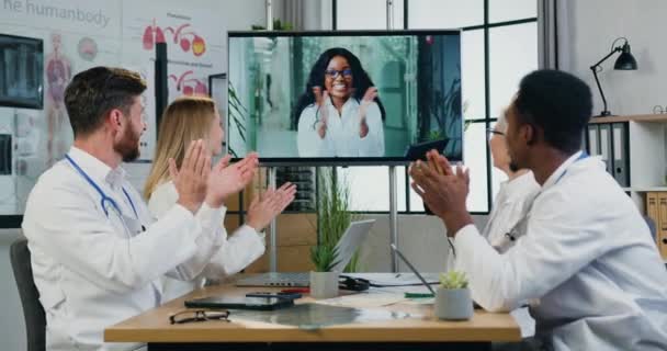 Красива усміхнена успішна жінка афроамериканського головного лікаря привітання з оплесками її професійної медичної команди під час онлайн-зустрічі, концепція медицини — стокове відео