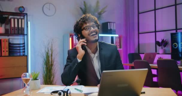 Attractive smiling successful bearded arabian office manager in formal wear has pleasant phone conversation during overtime work in evening office,front view — Stockvideo