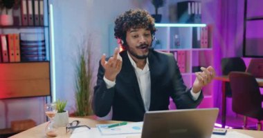 Çekici, başarılı, yetenekli, sakallı, kulaklıklı Müslüman iş adamı iş arkadaşlarıyla çevrimiçi sohbet ediyor ve etkili bir sondan sonra el çırpıyor.