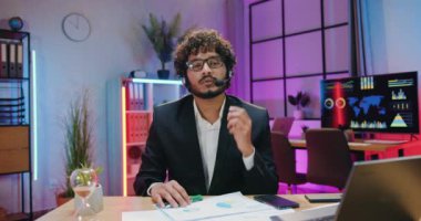 İş konsepti, kendine güvenen yetenekli Hintli bir ofis çalışanı kameranın önünde modern akşam çalışma odası geçmişiyle ilgili röportaj yaparken oturuyor.