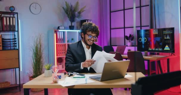 Likable cheerful contented successful bearded asian office manager rejoycing from good made work and scattering papers over his head in evening office — Vídeo de Stock